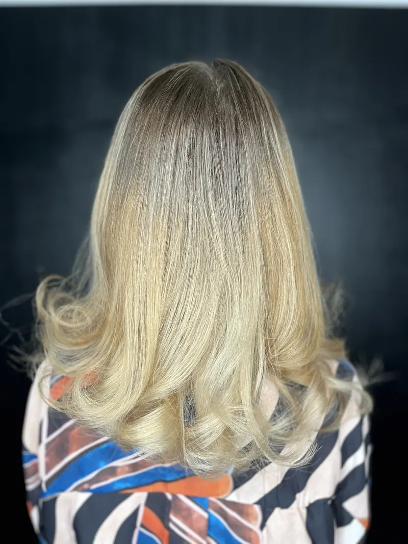 După: păr blond cald, cu rădăcina umbrită și bucle mari, din spate pe fundal negru
